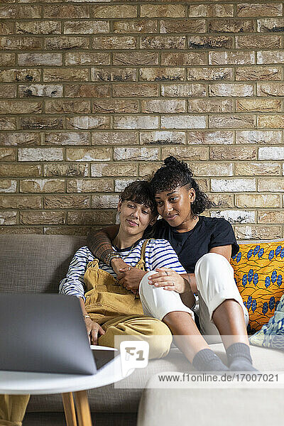 Lesbisches Paar  das zu Hause auf dem Sofa sitzt und den Laptop betrachtet