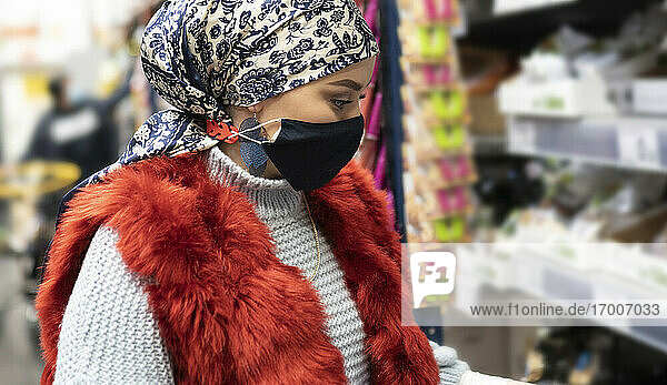 Junge Frau mit Kopftuch und Gesichtsschutzmaske beim Einkaufen im Supermarkt