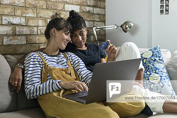 Frau mit Laptop und Kreditkarte in der Hand  während sie bei ihrer Freundin zu Hause sitzt