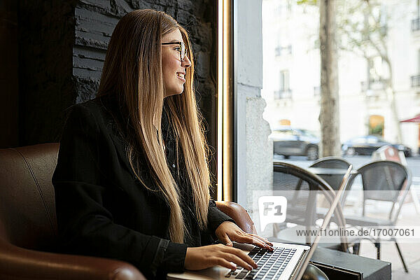 Lächelnde Frau  die wegschaut  während sie im Café sitzt und einen Laptop benutzt