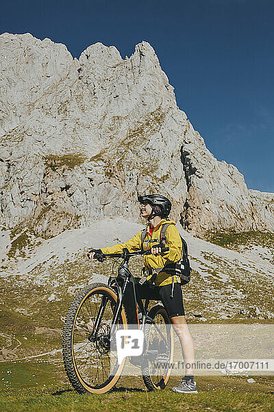 Female cyclist with bicycle against rock mountain at Picos de Europa National Park  Cantabria  Spain