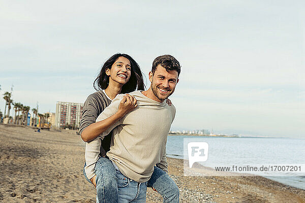 Smiling boyfriend while giving piggyback ride to girlfriend at beach