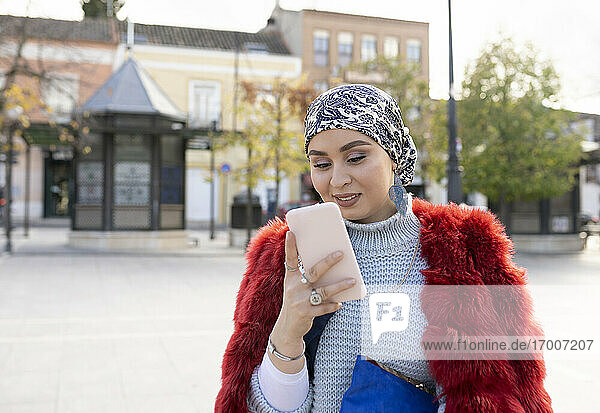 Junge Frau in warmer Kleidung  die ein Mobiltelefon benutzt  während sie in der Stadt steht