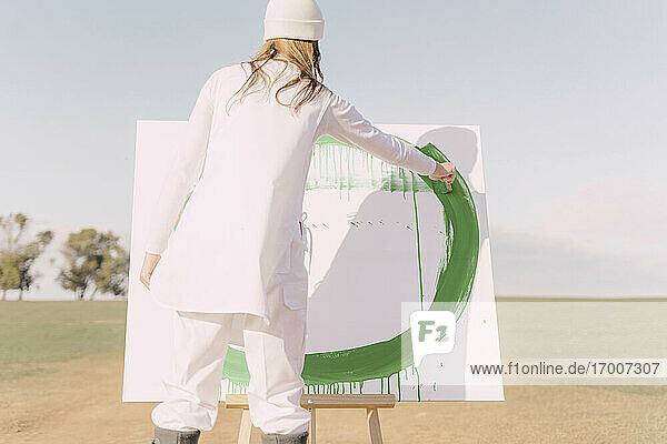 Junge Frau auf trockenem Feld  die eine Leinwand mit grüner Farbe bemalt
