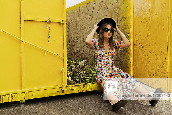 Woman wearing flower dress  sitting in yellow container  holding hat