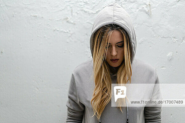 Mid adult woman with eyes closed wearing hood while standing against white wall