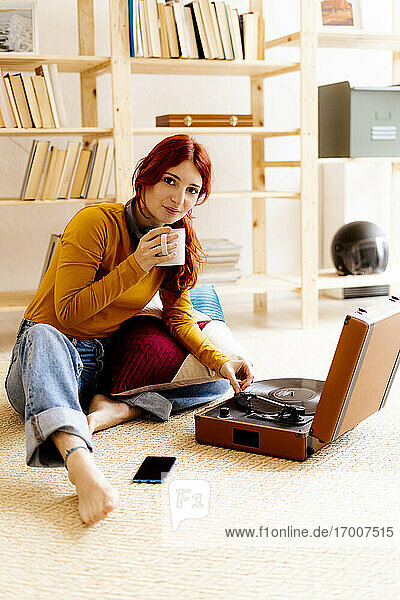Junge Frau trinkt Kaffee  während sie zu Hause am Plattenspieler sitzt