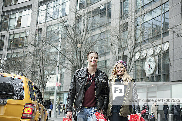 Lächelndes Paar mit Einkaufstaschen beim Spaziergang auf der Straße in der Stadt