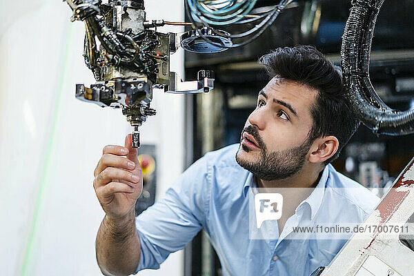 Männlicher Unternehmer konzentriert sich bei der Analyse eines Roboterarms in einer Produktionsstätte