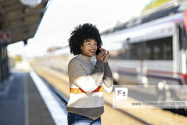 Glückliche Frau  die mit ihrem Handy telefoniert  während sie am Bahnhof wartet
