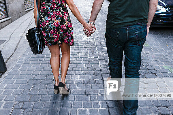 Freundin und Freund halten Hände auf der Straße in der Stadt gehen