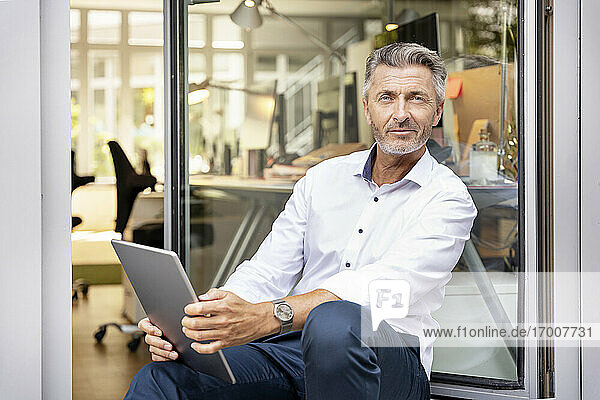 Älterer Geschäftsmann mit digitalem Tablet an der Bürotür sitzend