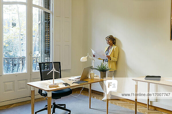 Geschäftsfrau prüft Bauplan  während sie im Büro an der Wand steht