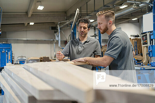 Zwei Zimmerleute prüfen Holzbretter in der Produktionshalle