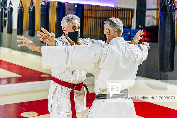 Männer mit ausgestreckten Armen  die Gesichtsmasken tragen  während sie im Fitnessstudio Karate üben