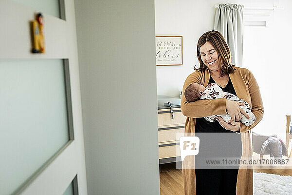 Smiling mother carrying newborn baby while standing in nursery
