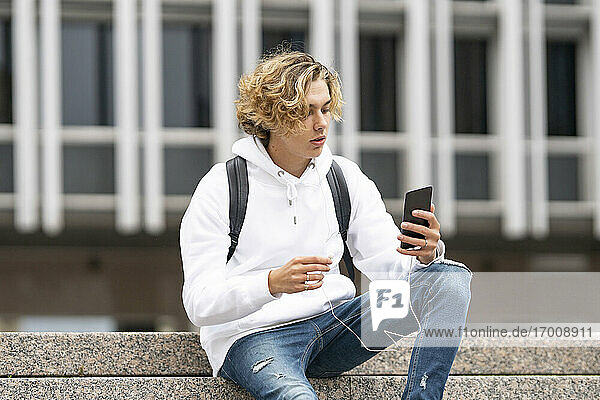 Junger Mann  der ein Mobiltelefon benutzt  während er auf einer Treppe sitzt