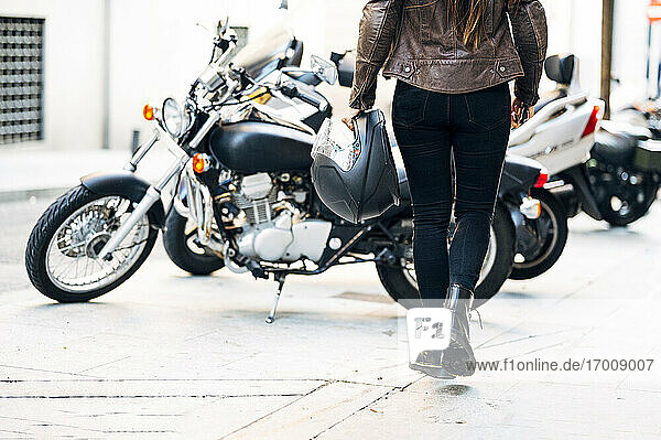 Motorradfahrerin mit Helm  die auf dem Bürgersteig in der Stadt auf ein Motorrad zugeht