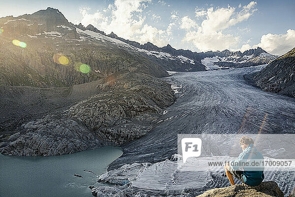 Switzerland  Valais  Obergoms  Man sitting on rock  overlooking Rhone Glacier and mountains