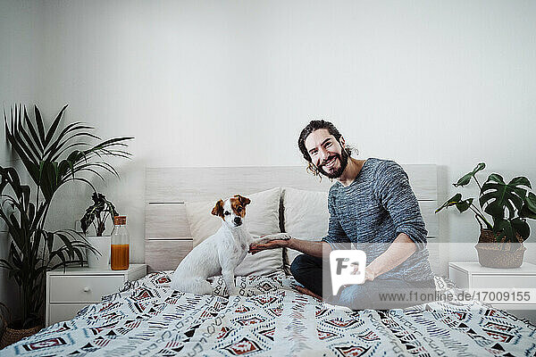 Gut aussehender Mann spielt mit Hund  während er zu Hause auf dem Bett sitzt