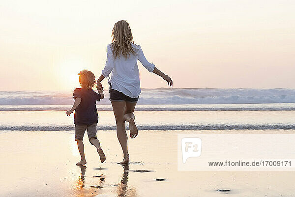Mother holding hand of son while running toward sea during sunset