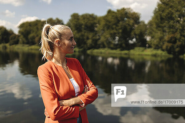 Female entrepreneur with arms crossed looking away while standing by lake