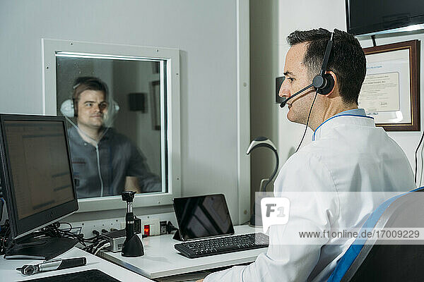 Männlicher Audiologe bei der Untersuchung eines Patienten mit Kopfhörern in der Klinik