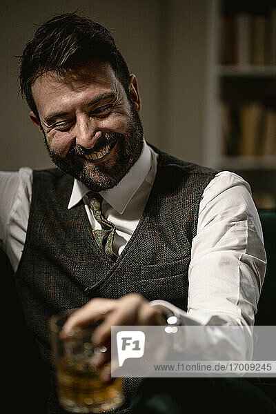 Portrait of bearded man laughing while enjoying glass of whiskey