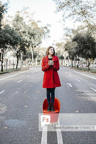 Junge Frau mit geschlossenen Augen  die eine Kaffeetasse hält  während sie auf einem Sitz auf der Straße steht