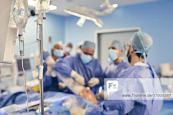 IV-Tropf im Operationssaal mit Ärzten  die eine Operation durchführen  im Hintergrund