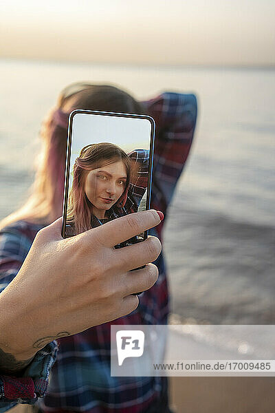 Junge Frau nimmt Selfie durch Handy am Strand