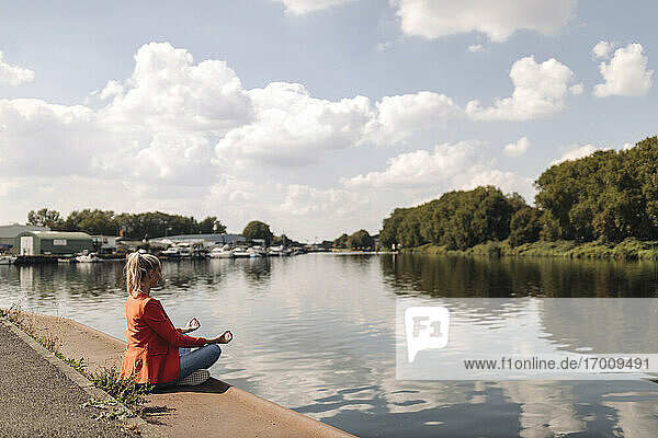 Businesswoman meditating at lakeshore against sky