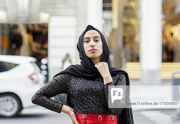 Portrait of young beautiful woman wearing black hijab posing in middle of street with hand on hip