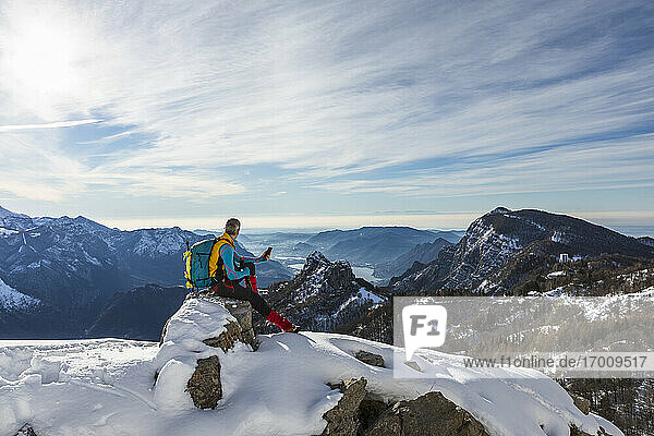 Männlicher Wanderer  der sein Handy benutzt  während er auf einem Berg gegen den Himmel sitzt  Orobic-Alpen  Lecco  Italien