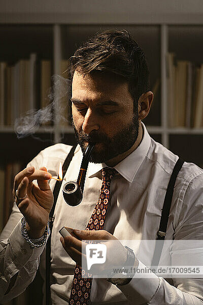 Portrait of bearded man lighting smoking pipe with match