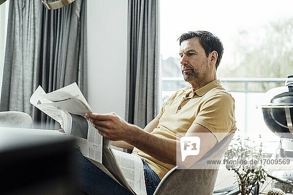 Mature man reading newspaper in living room at home