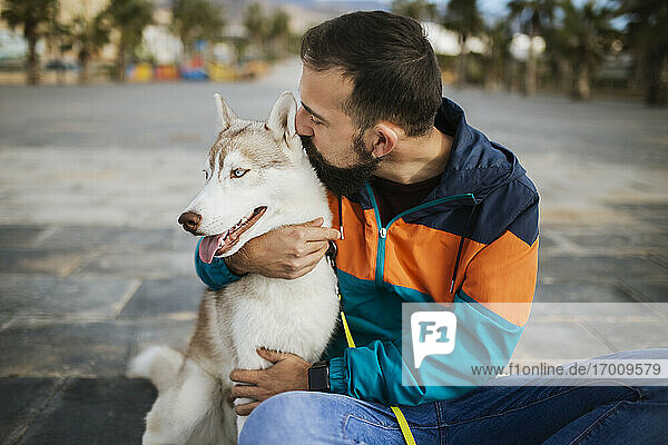 Bärtiger Mann küsst Siberian Husky  während er auf der Straße sitzt