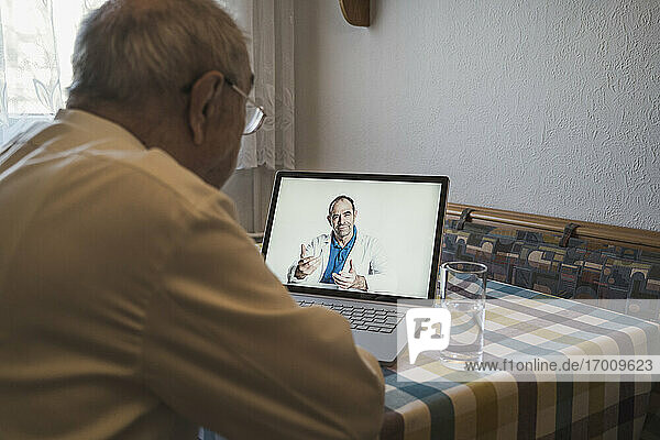Senior man taking advice from male general practitioner through laptop on video call at home