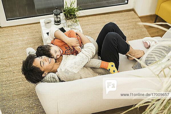 Smiling mother embracing son while resting on sofa at home