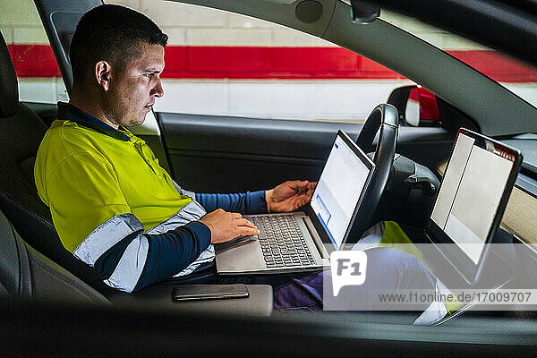 Male technician working on laptop for programming in electric car