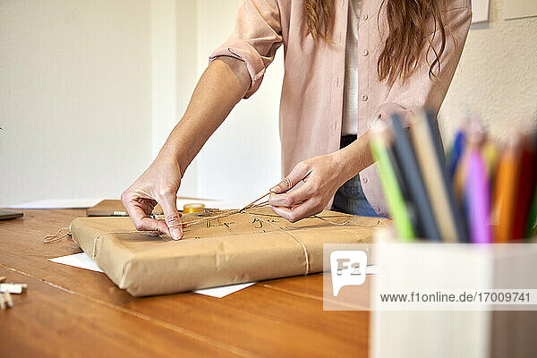 Weibliche Freiberuflerin bereitet die Auslieferung eines Pakets vor  indem sie einen Knoten aus einer Schnur im Wohnzimmer bindet