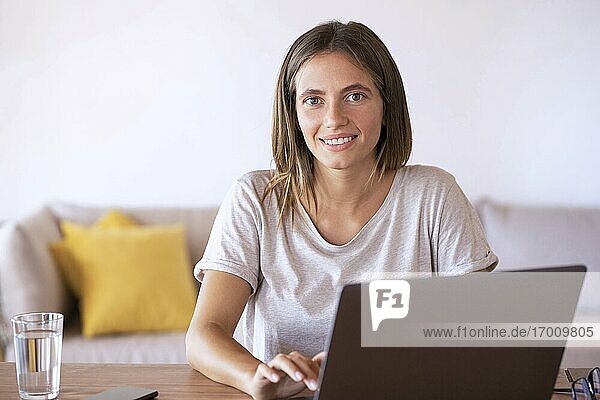 Lächelnde weibliche Fachkraft  die einen Laptop bei der Arbeit zu Hause benutzt