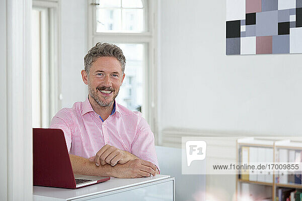 Smiling mature male professional by laptop at desk in office cabin