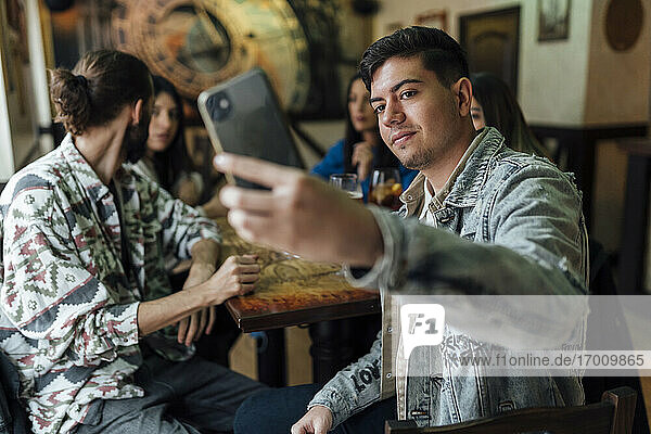 Junger Mann nimmt Selfie mit Freunden durch Mobiltelefon im Restaurant