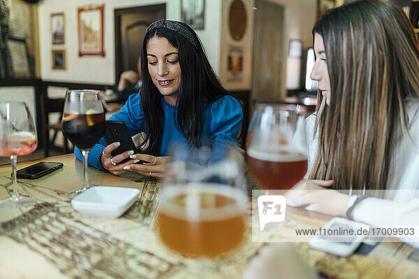 Frau  die ein Mobiltelefon benutzt  sitzt neben ihrer Freundin im Restaurant
