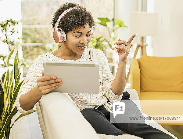 Frau mit digitalem Tablet hört Musik über Kopfhörer  während sie zu Hause auf dem Sofa sitzt