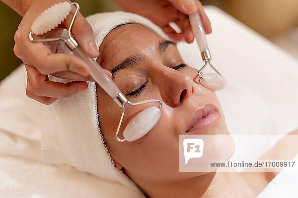Young female customer receiving facial massage during spa treatment from beautician