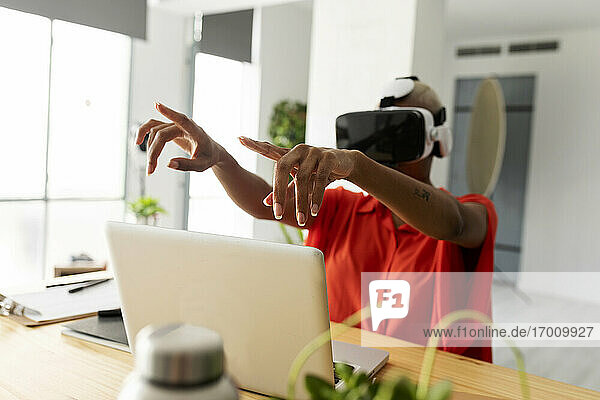 Frau sitzt am Schreibtisch mit Laptop und benutzt eine VR-Brille im Büro