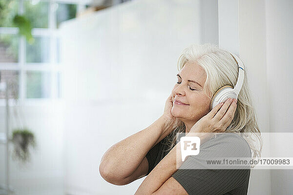 Entspannte ältere Frau  die in ihrer Wohnung Musik über Kopfhörer genießt