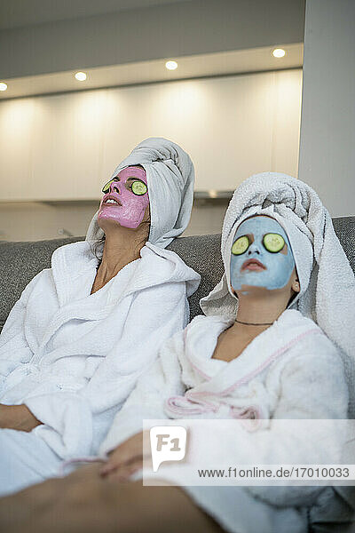 Mutter und Tochter mit Gesichtsmasken entspannen sich im Wohnzimmer